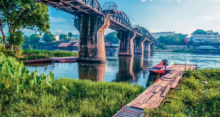 Pont historique en acier enjambant une rivière tranquille avec jetée en bois et végétation luxuriante