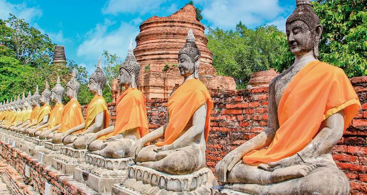 Longue rangée de statues de Bouddha en pierre drapées de robes orange devant des stupas en brique