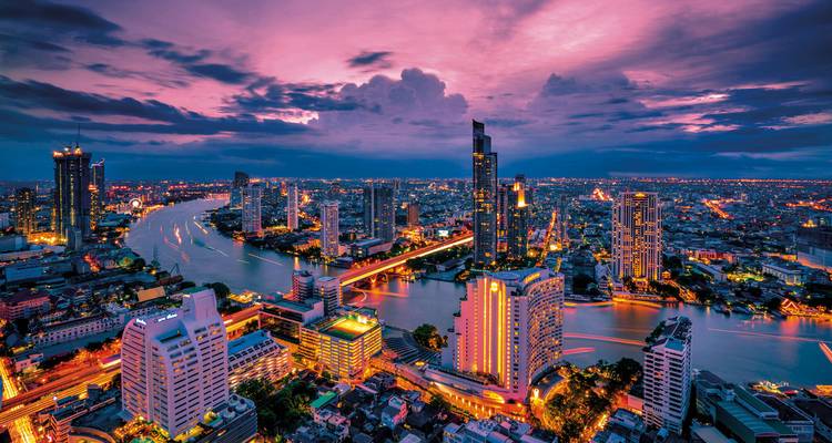 Luftaufnahme einer Stadtlandschaft in der Dämmerung mit Lichtern, die die Gebäude beleuchten.
