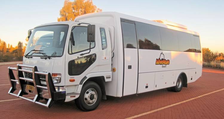 Autocar de tourisme blanc garé sur un pavé de briques rouges.