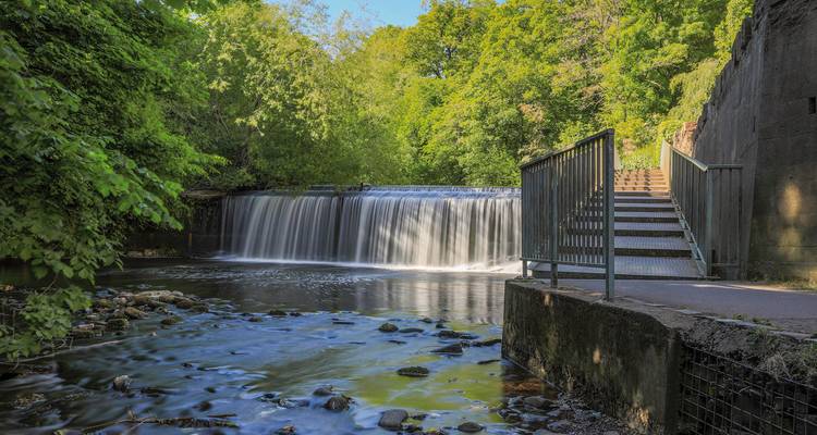 Wasserfall mit umgebender Vegetation und einer Fußgängerbrücke.