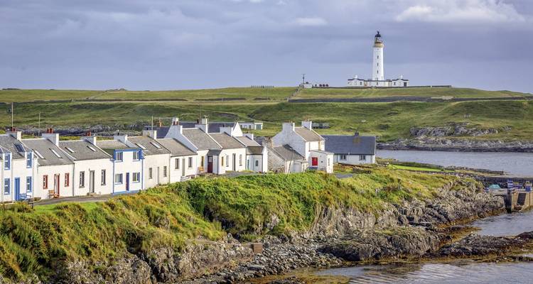 Pueblo costero con casas blancas y un faro en la distancia.