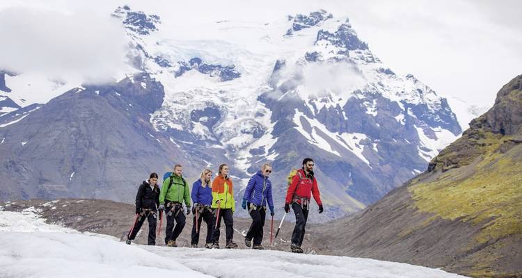Groupe de randonneurs sur un glacier avec des montagnes en arrière-plan.