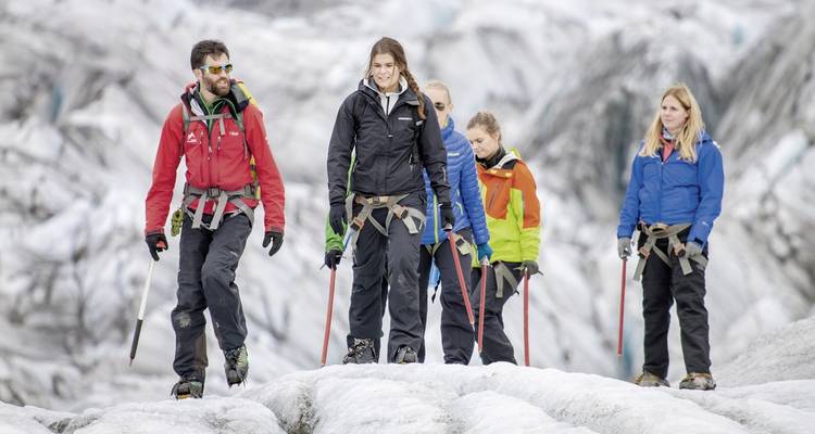Groep wandelaars op een gletsjer met besneeuwde toppen op de achtergrond.