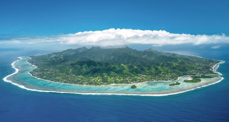 Vista aérea de una isla tropical con montañas exuberantes rodeada por un arrecife vibrante.