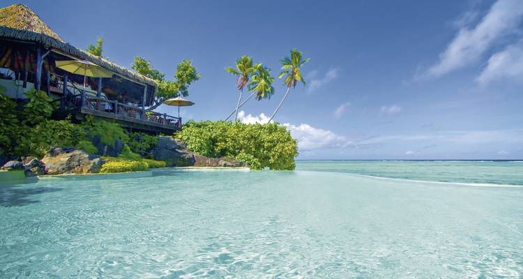 Escena relajante con bungalows frente a la playa y palmeras en una playa turquesa.