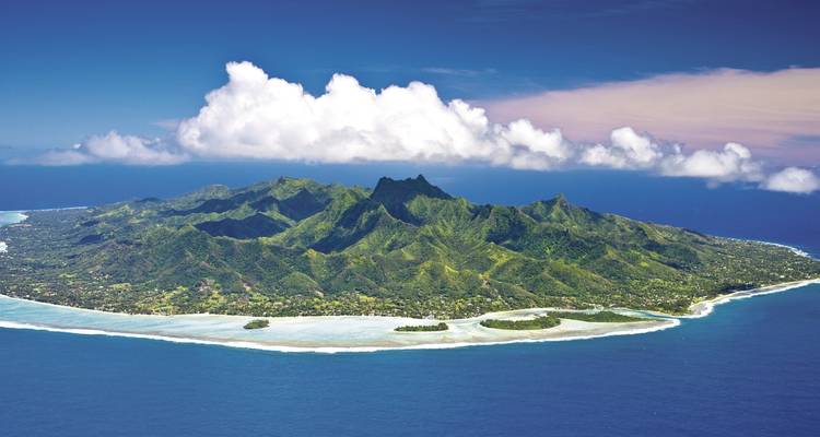 Isla montañosa con vegetación exuberante rodeada de aguas oceánicas cristalinas.