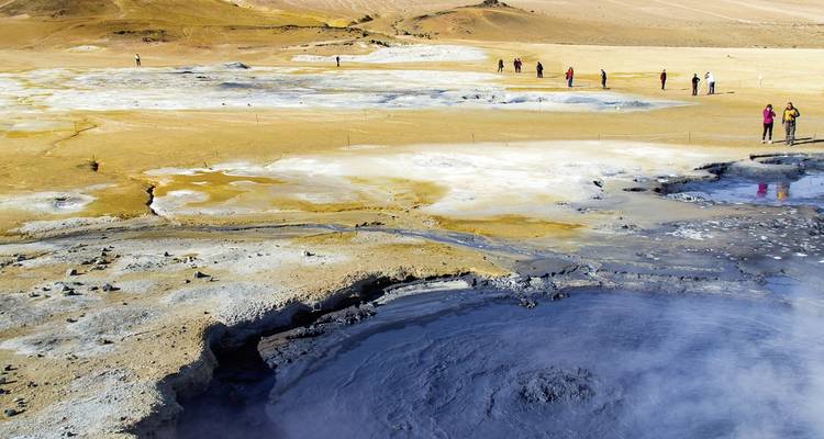 Zone géothermique avec de la boue bouillonnante et des personnes qui marchent.
