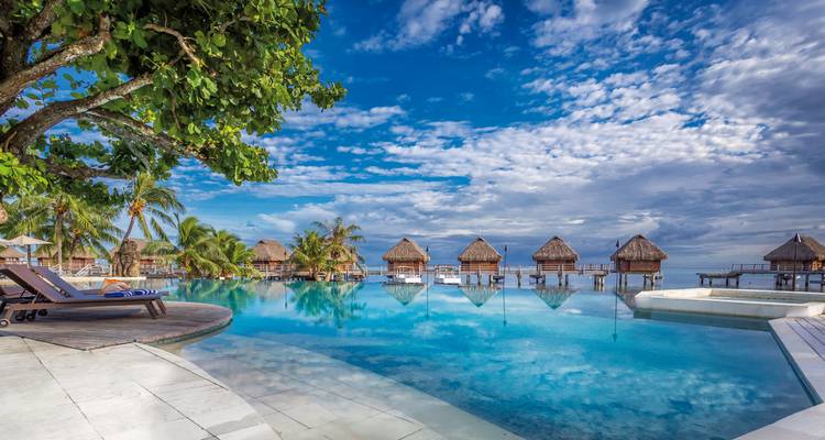 Bungalows sur pilotis et piscine à débordement dans un complexe tropical.