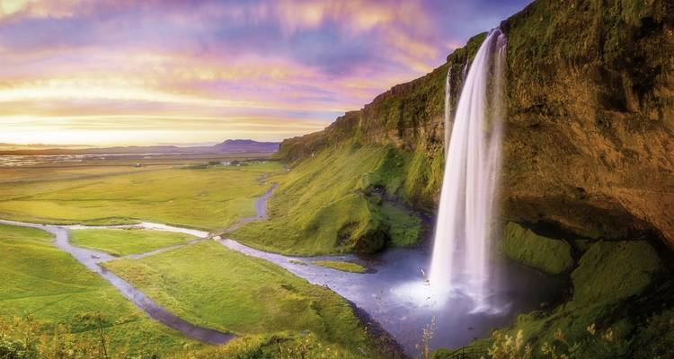 Une haute cascade dévalant d'une falaise dans un paysage herbeux avec un ciel vibrant.
