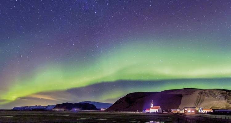 Aurores boréales au-dessus d'une église et de petits villages avec des montagnes en arrière-plan.