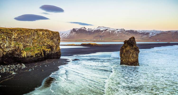 Une côte rocheuse avec de grandes arches marines contre un ciel coloré.