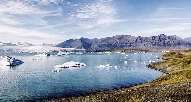 Un lac avec des icebergs et des montagnes couvertes de glaciers au loin.