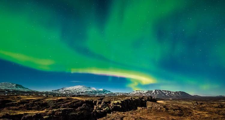 Nordlichter tanzen über schneebedeckte Berge und Lavafelder in der Nacht.