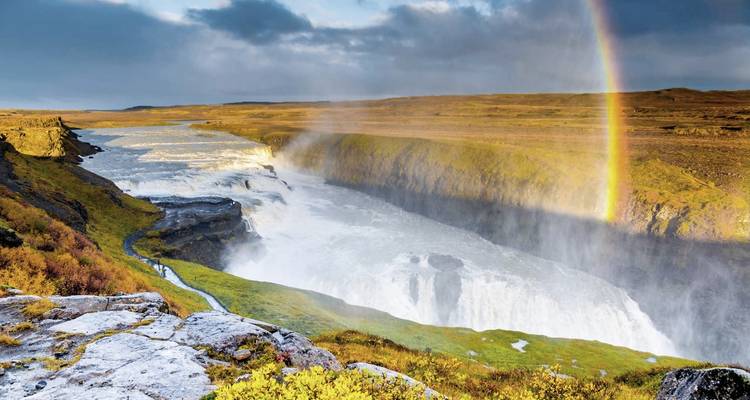 Wasserfall mit Regenbogen über einer zerklüfteten Landschaft.