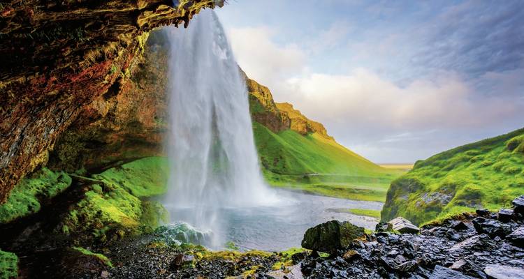 Wasserfall-Blick von hinter üppig grüner Felswand.