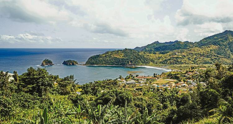 Een weelderige, groene kustplaats omgeven door bergen en oceaan.