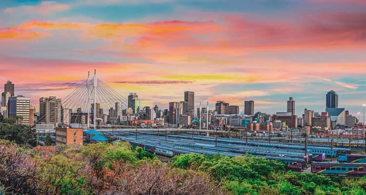 Farbenfroher Sonnenuntergang über der Johannesburger Skyline mit der Nelson-Mandela-Brücke und Bahnhöfen