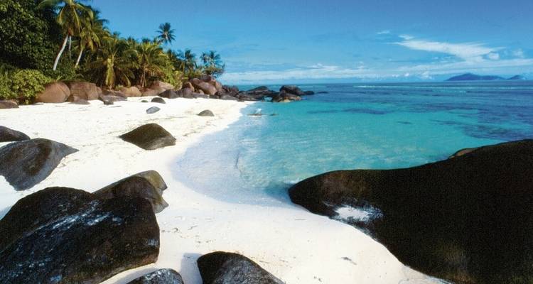 Plage de sable avec une eau turquoise claire et de gros rochers.