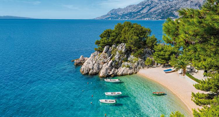 A stunning beach with clear water and small boats near a rocky outcrop.