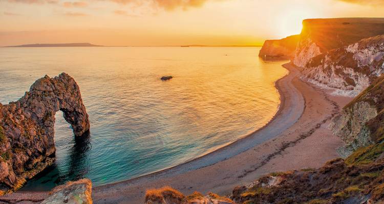 Durdle Door rotsformatie bij zonsondergang met uitzicht op het strand.