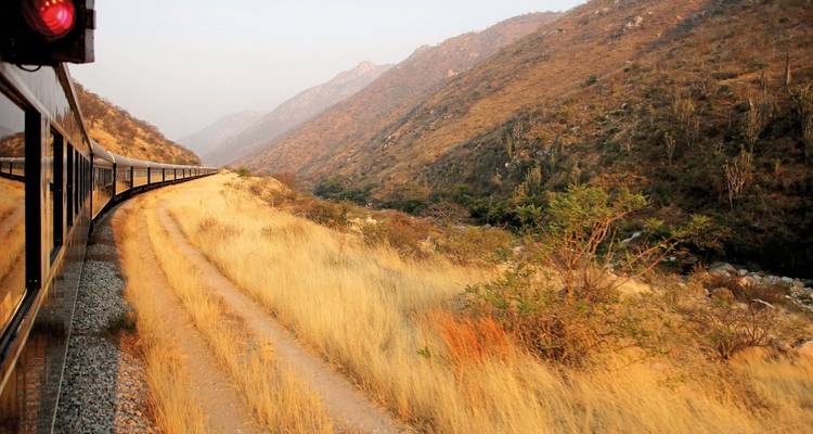 Tren de lujo viajando a través de un paisaje montañoso árido.