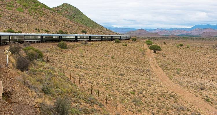 Tren de lujo viajando a través de una región montañosa árida.