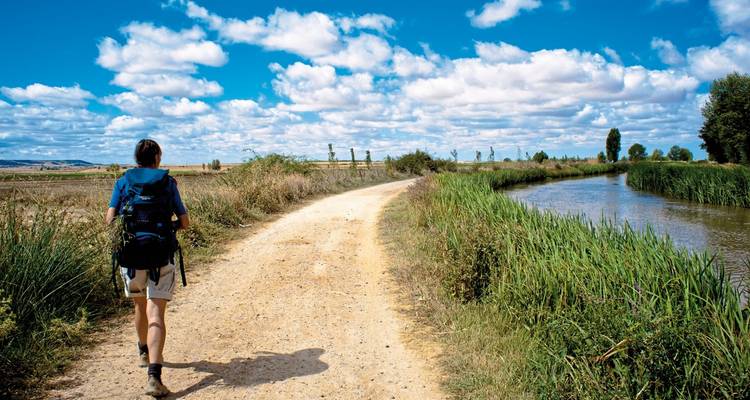 Wandelaar die langs een zandpad naast een kanaal loopt.