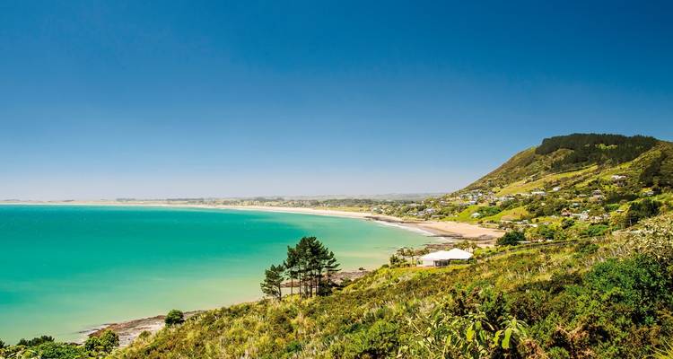 Küstenlandschaft mit türkisblauem Ozean und grünen Hügeln.
