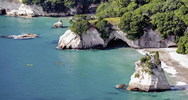 Falaises côtières avec formations rocheuses naturelles et personnes faisant du kayak.