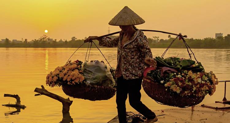 Person, die Körbe entlang eines Flusses bei Sonnenuntergang trägt.