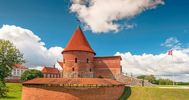 Mittelalterliche Burg aus roten Ziegeln mit einem runden Turm unter blauem Himmel.