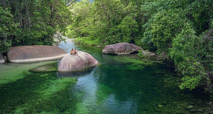 Deux personnes assises sur un gros rocher dans une rivière.