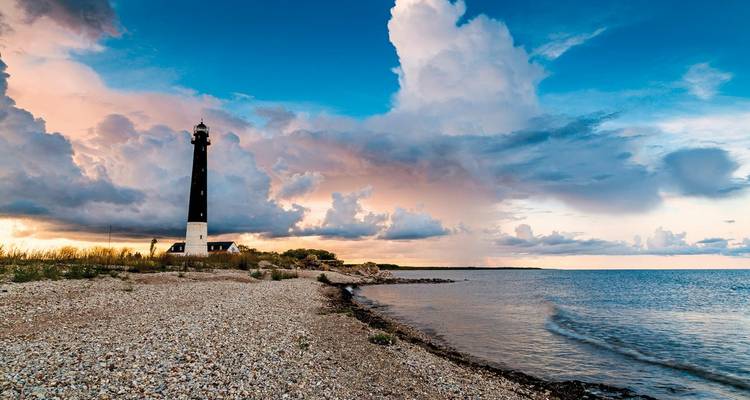 Vuurtoren aan de kust met dramatische wolken bij zonsondergang.