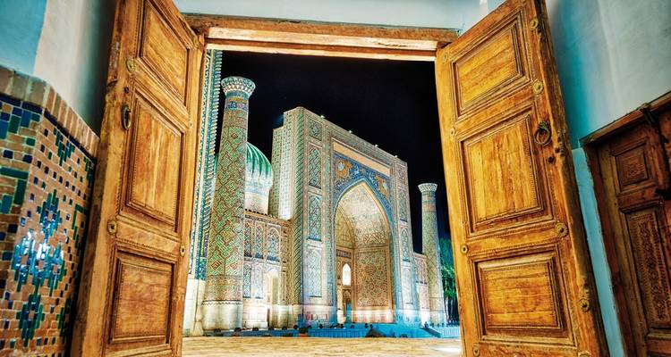Ornate blue-tiled mosque seen through wooden doors at night.