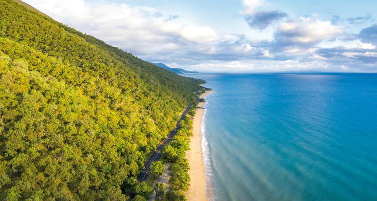 Luchtfoto van een lang, zandig strand omringd door weelderige groene bergen.