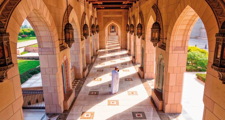 Un homme en tenue traditionnelle se tient dans le couloir orné d'une mosquée.