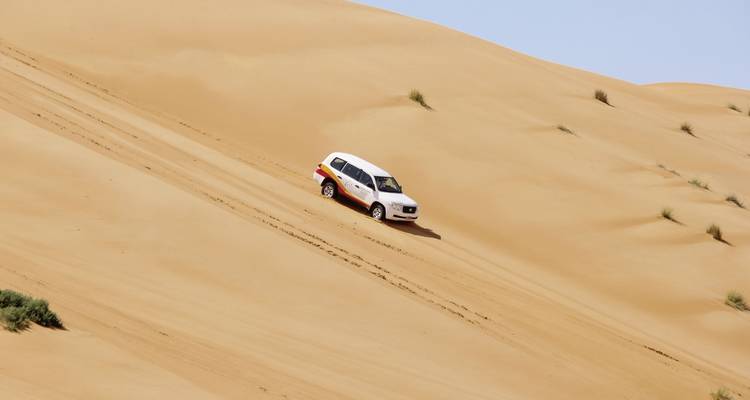 Un véhicule descend une grande dune de sable dans un désert.