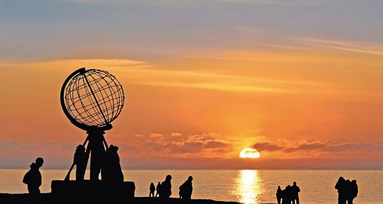 Silhouetted globe sculpture with people at sunset over the sea.