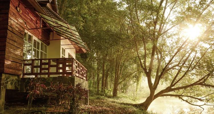 Maison au bord d'une rivière paisible entourée d'arbres au lever du soleil.