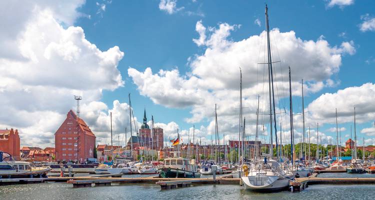 Marina avec voiliers amarrés et horizon d'une ville historique en arrière-plan.