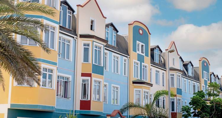 Reihe von pastellfarbenen deutschen Stadthäusern im deutschen Stil mit Palmen in einer teilweise bewölkten Umgebung in Swakopmund.