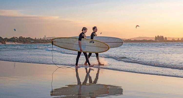Two surfers walking along the beach at sunset with surfboards.