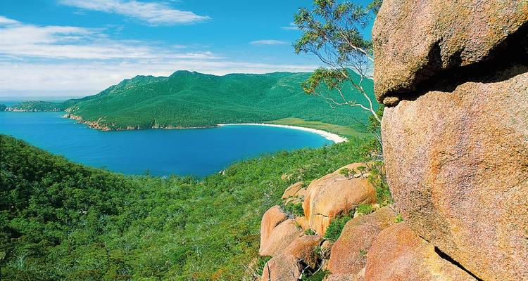 Küstenblick mit klarem Wasser, grünen Hügeln und Felsen.