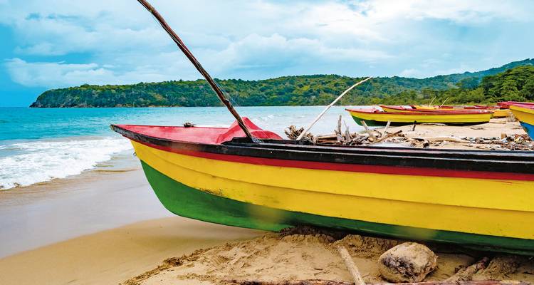 Colorful boats on a sandy beach with lush hills.