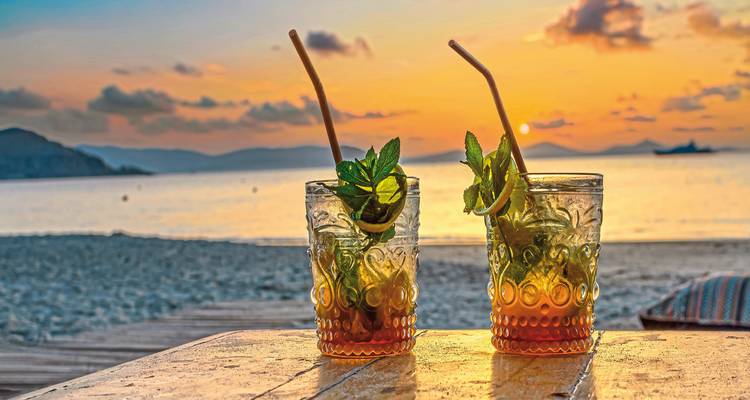 Tropical drinks with mint leaves on a beach at sunset.
