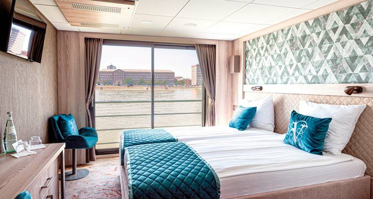 Cabin with large windows and twin beds offering a view of the river and buildings.