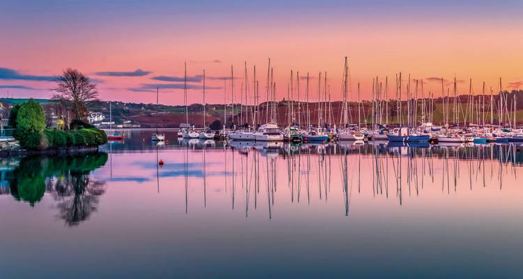 A harbor with boats at sunset, reflecting on the calm water.