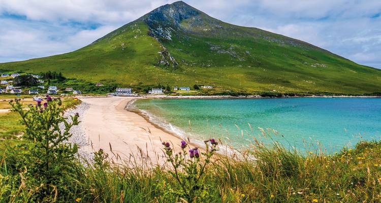 Plage avec une montagne en arrière-plan et quelques maisons le long du rivage.