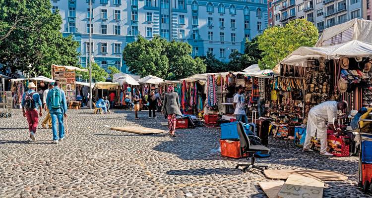 Market scene with various stalls and people shopping in an open-air setting.